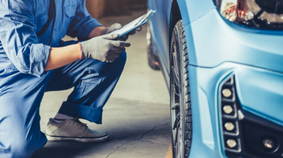 Car mechanic technician holding clipboard and conducting vehicle maintenance in car dealership garage.
