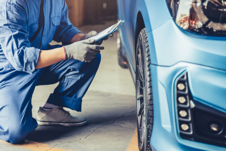 Car mechanic technician holding clipboard and conducting vehicle maintenance in car dealership garage.